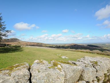 A grassy landscape with hills and a stone wall under a blue sky at Cheesewring Cottage in Minions near Upton Cross