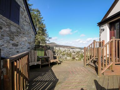 A wooden patio with two chairs a small table stone wall and steps leading to a door at Cheesewring Cottage in Minions near Upton Cross