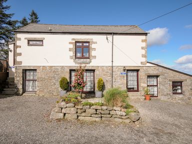A stone and stucco building with multiple windows and a small garden bed in front at Cheesewring Cottage in Minions near Upton Cross