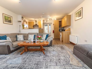 A living room with a sectional sofa a wooden coffee table and a kitchen area at Cheesewring Cottage in Minions near Upton Cross