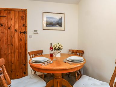 A wooden dining table set for two with plates glasses and cutlery and flower vase in a room with wooden door and framed picture at Cheesewring Cottage in Minions near Upton Cross