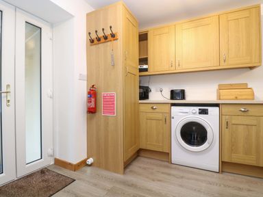 A utility room with washing machine wooden cabinets fire extinguisher and double glass door at Cheesewring Cottage in Minions near Upton Cross