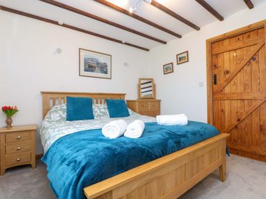 A bedroom with a wooden bed and blue bedding with towels on it at Cheesewring Cottage in Minions near Upton Cross