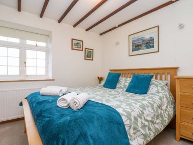 A bedroom with a wooden bed frame blue pillows and a floral duvet near a window at Cheesewring Cottage in Minions near Upton Cross