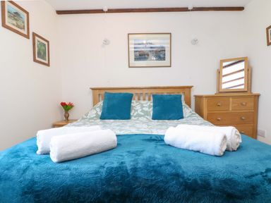 A bedroom with a wooden bed and dresser with towels on the bed at Cheesewring Cottage in Minions near Upton Cross