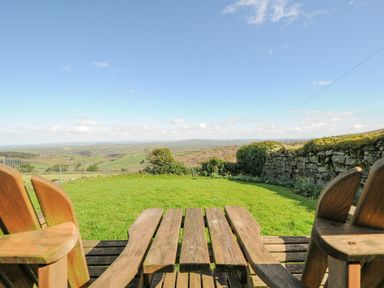 A garden with wooden chairs and table overlooking a countryside view at Fizz-Gog Cottage in Minions near Upton Cross