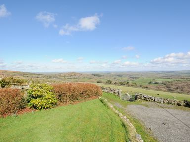A garden with bushes and stone walls overlooking fields and hills at Fizz-Gog Cottage in Minions near Upton Cross