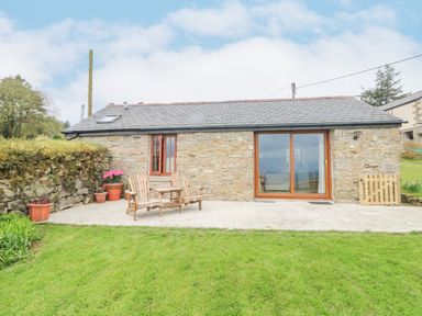 A stone cottage with wooden chairs on a patio and potted plants on grass at Fizz-Gog Cottage Minions near Upton Cross