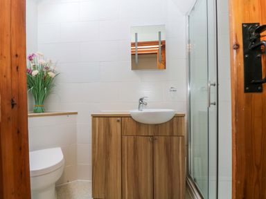 A bathroom with a wooden vanity cabinet with a sink toilet flowers in a vase and a glass shower enclosure at Fizz-Gog Cottage Minions near Upton Cross