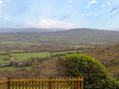 A landscape view of fields and hills with a wooden fence and bushes in the foreground at Fizz-Gog Cottage in Minions near Upton Cross