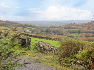 A rural landscape with stone walls bushes and a metal gate at Fizz-Gog Cottage in Minions near Upton Cross