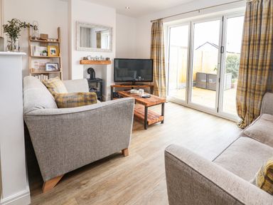 A living room with two sofas a wooden coffee table a television and sliding glass doors at 6 Cwrt Griffiths in Prestatyn