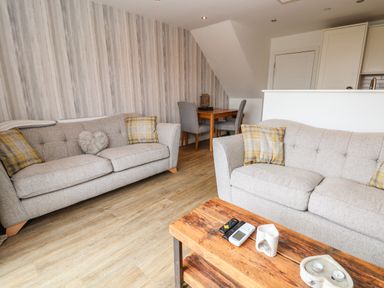 A living room with two gray sofas and a wooden coffee table with remotes and decorative items at 6 Cwrt Griffiths in Prestatyn