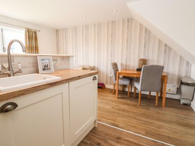 A kitchen area with a wooden countertop and white sink next to a small dining table with two upholstered chairs at 6 Cwrt Griffiths in Prestatyn