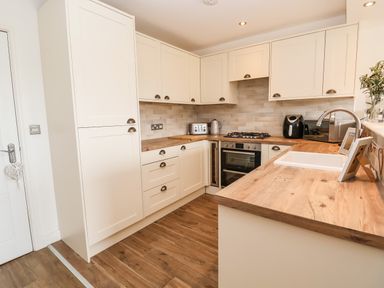 A kitchen with cream cabinets wooden countertops a gas stove an oven toaster kettle and a sink at 6 Cwrt Griffiths in Prestatyn