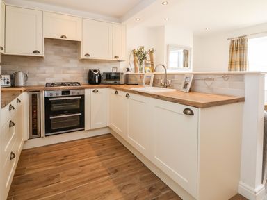 A kitchen with wooden countertops white cabinets an oven a sink and small appliances at 6 Cwrt Griffiths Prestatyn