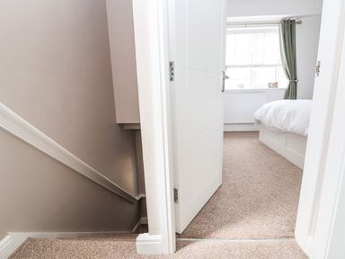 A hallway with carpeted stairs and an open door leading to a bedroom with a bed near a window at 6 Cwrt Griffiths in Prestatyn