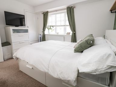 A bedroom with a bed a television on a white chest of drawers and a window with green curtains at 6 Cwrt Griffiths in Prestatyn