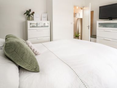 A bedroom with a white bed and green pillows two white dressers a television and a door leading to another room at 6 Cwrt Griffiths in Prestatyn
