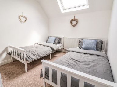 A bedroom with two single beds with gray bedding and pillows and heart-shaped wall decorations at 6 Cwrt Griffiths in Prestatyn