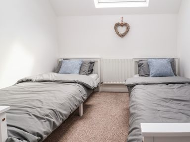 A bedroom with two single beds with gray bedding and blue pillows at 6 Cwrt Griffiths in Prestatyn