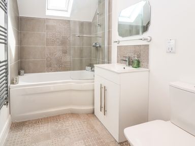 A bathroom with a bathtub shower combination a sink with vanity a toilet and patterned tiles at 6 Cwrt Griffiths in Prestatyn