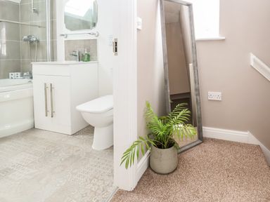 A bathroom with a bathtub shower toilet and sink next to a hallway with a plant and a standing mirror at 6 Cwrt Griffiths in Prestatyn