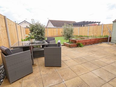 A fenced backyard with patio furniture a glass table a small plant raised garden beds and artificial grass at 6 Cwrt Griffiths in Prestatyn