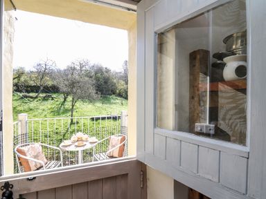 A small balcony with a table set for tea and two chairs with cushions overlooking a grassy area with trees at The Cheese Loft in White Mill near Carmarthen