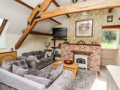 A living room with wooden beams sofas a brick fireplace and a television at The Cheese Loft in White Mill near Carmarthen