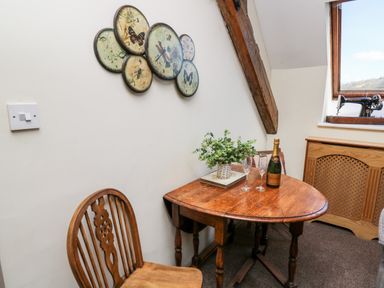 A small wooden table with a plant, two glasses and a bottle on it next to a wooden chair and a window with a sewing machine on the sill at The Cheese Loft in White Mill near Carmarthen