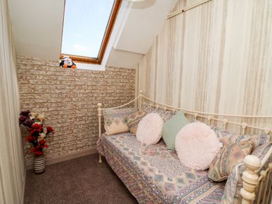 A small room with a daybed with patterned cushions skylight and a vase with red and white flowers at The Cheese Loft in White Mill near Carmarthen