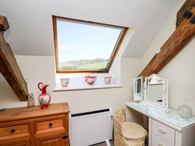 A room with a wooden dresser and porcelain vases next to a window and a white dressing table with a mirror and cushioned chair at The Cheese Loft White Mill near Carmarthen