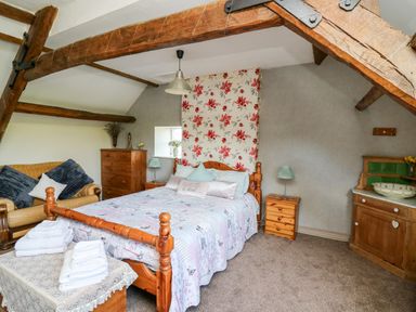 A bedroom with a wooden bed a floral wallpaper behind the bed a sofa a chest of drawers and a small cabinet at The Cheese Loft in White Mill near Carmarthen