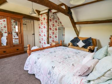 A bedroom with a wooden bed and wardrobe a small couch with cushions and floral wallpaper at The Cheese Loft White Mill near Carmarthen