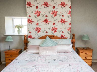 A bedroom with a wooden bed with pillows and floral wallpaper behind at The Cheese Loft in White Mill near Carmarthen