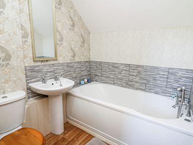 A bathroom with a white bathtub a pedestal sink a toilet with a wooden seat and a wall mirror at The Cheese Loft in White Mill near Carmarthen