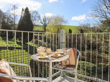 A small outdoor balcony with a round table set with a teapot cups and plates of biscuits and two metal chairs with cushions at The Cheese Loft in White Mill near Carmarthen