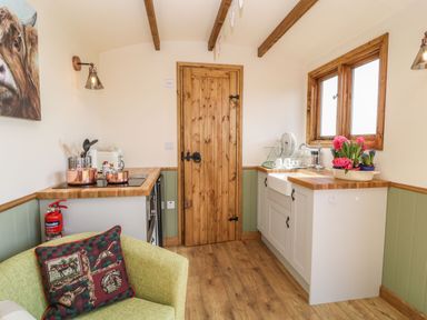A kitchen with wooden countertops a sink with flowers on the counter a stove with copper pots and a green armchair at Tawny in Morchard Bishop