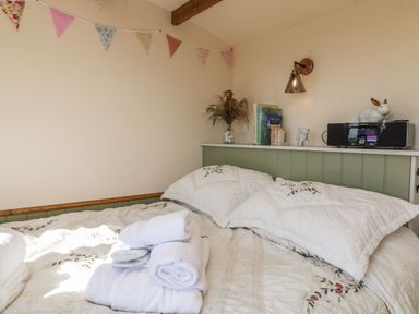 A bedroom with a bed with embroidered bedding and folded towels on it and a shelf with books a vase with dried flowers and a radio at Tawny in Morchard Bishop