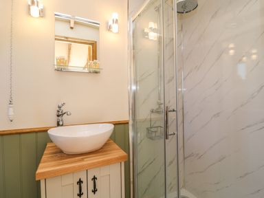 A bathroom with a white vessel sink on a wooden countertop a wall mirror and a glass shower enclosure at Tawny in Morchard Bishop
