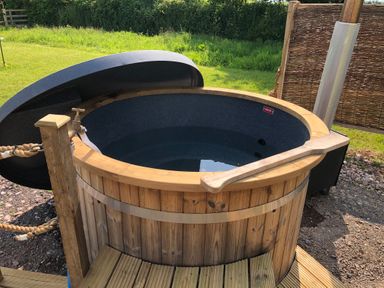 A wooden hot tub with water and a wooden paddle outside on a deck at Tawny in Morchard Bishop