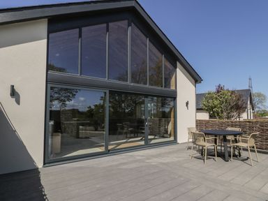 A patio with a round table and four chairs outside a building with large glass windows at The Barn in Llanfechell
