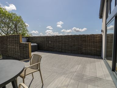An outdoor patio area with a round table and chairs with wicker fencing at The Barn in Llanfechell