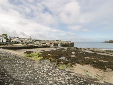 A coastal scene with boats moored near a stone pier and houses along the shoreline at The Barn in Llanfechell