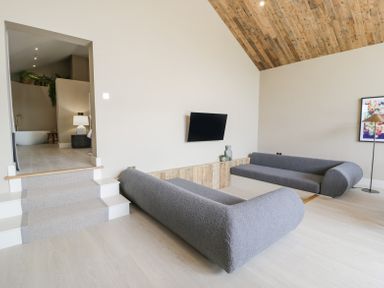 A living room with two gray sofas a wall mounted TV and wooden ceiling at The Barn in Llanfechell