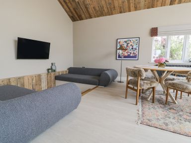 A living room with two gray sofas a wooden dining table with four chairs and a floral painting at The Barn in Llanfechell