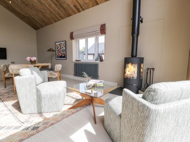 A living room with two armchairs a glass coffee table a wood-burning stove and a dining table at The Barn in Llanfechell