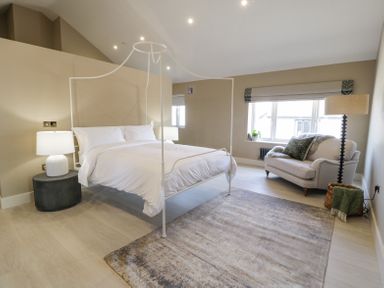 A bedroom with a white four-poster bed a gray rug a small sofa and floor lamp at The Barn in Llanfechell