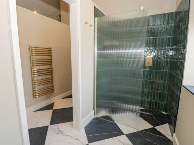 A bathroom with a glass shower screen green tiles and black and white checkered floor at The Barn in Llanfechell